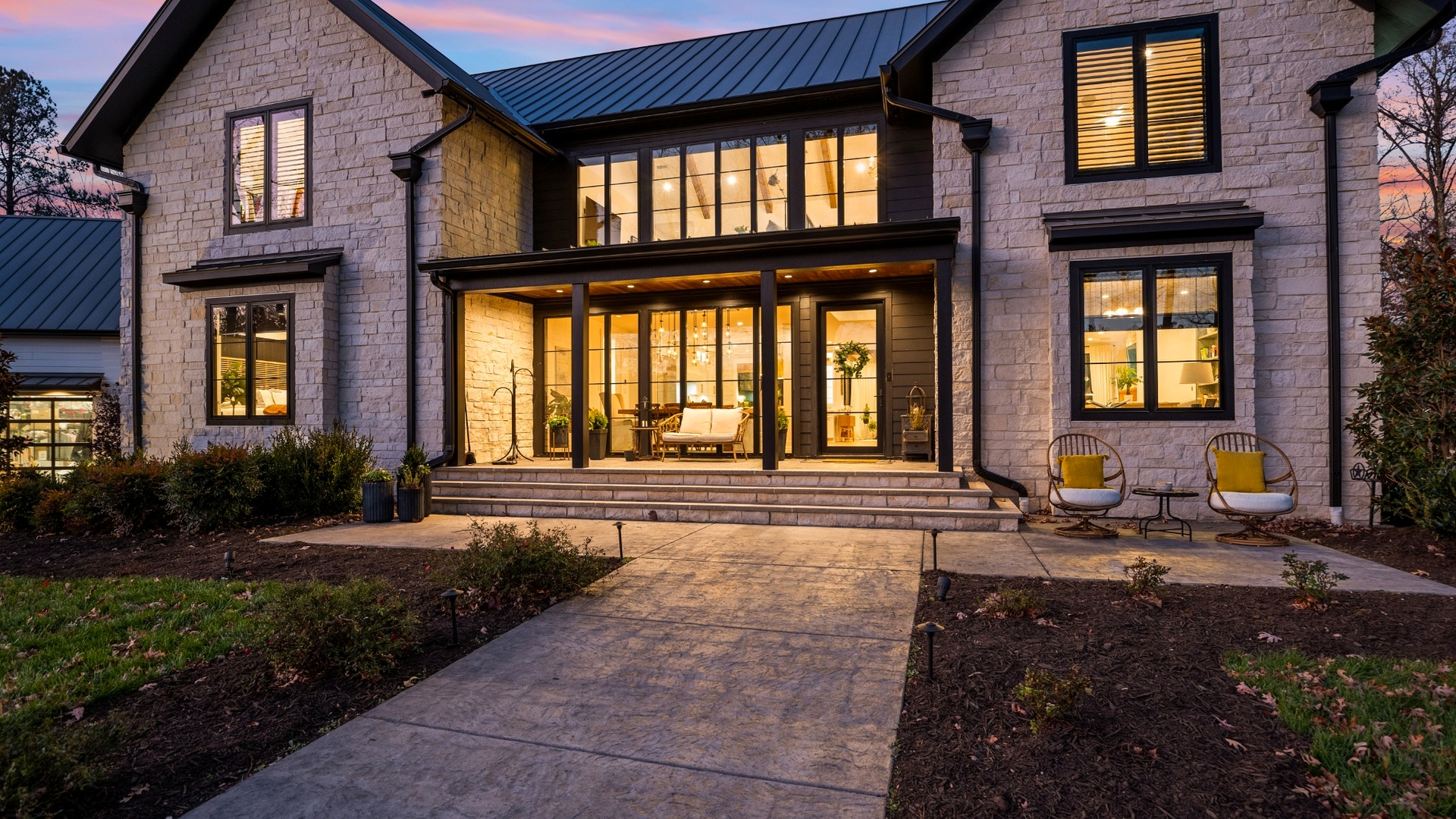 A Custom Homes Near Me stone home with warm windows and a covered porch at dusk